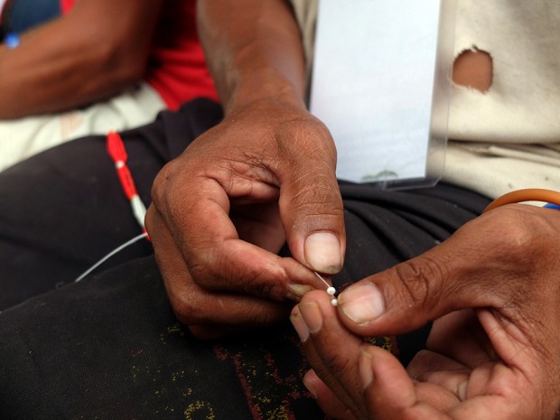 A Manobo farmer's thick fingers are deft enough to hold the tiny glass beads and thread them through fine strings.