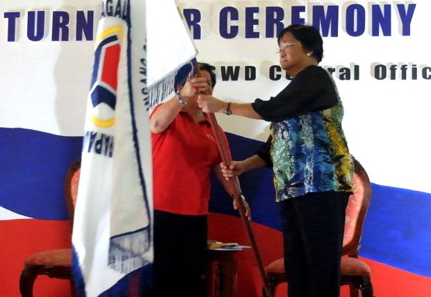 Secretary Taguiwalo receives the DSWD flag from her predecessor Corazon Soliman at last Friday's turn over ceremony.